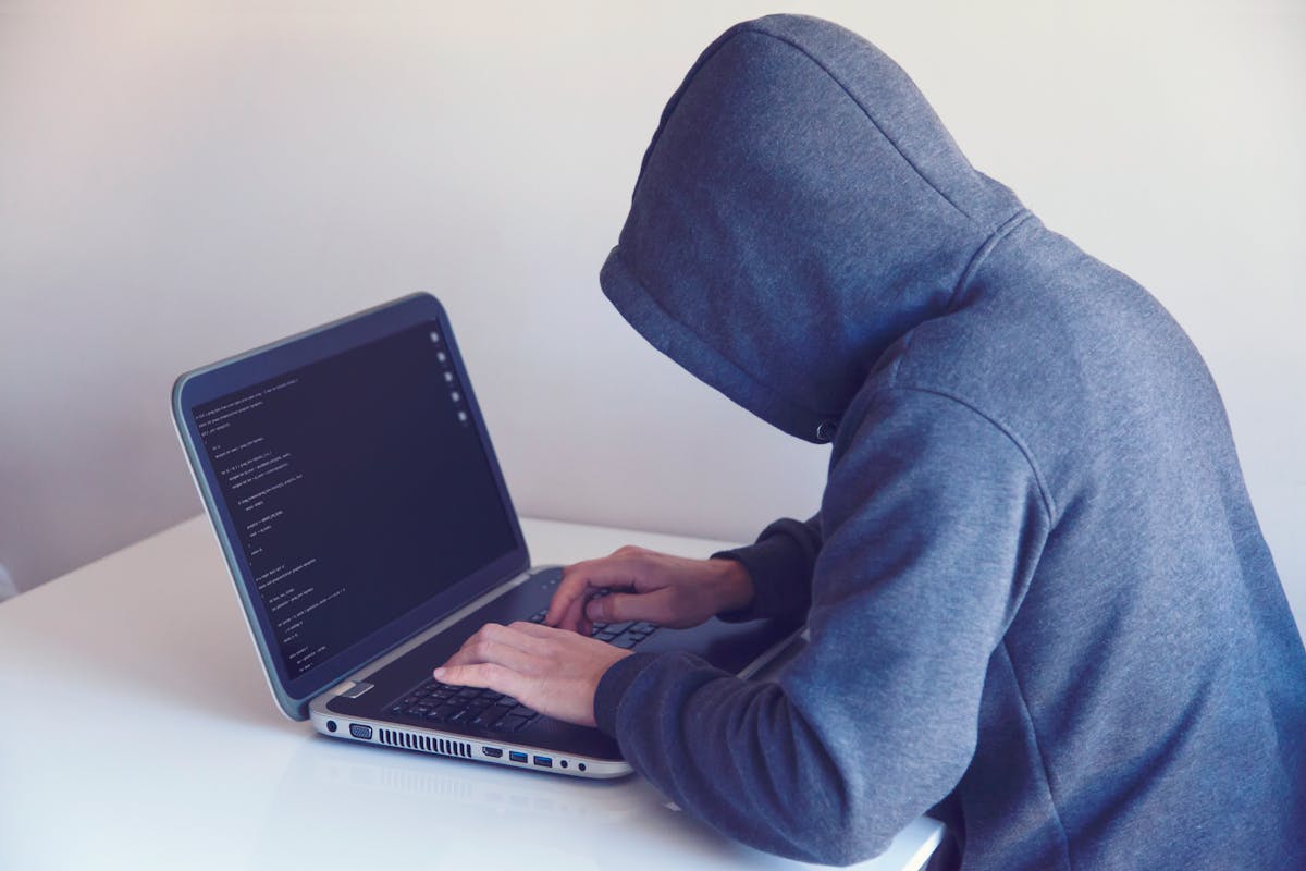 Anonymous hacker with on laptop in white room